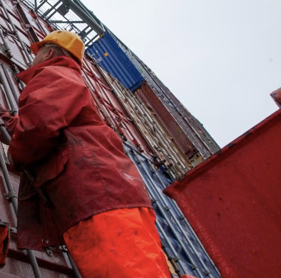 Port worker in a hard hat securing stacked cargo containers